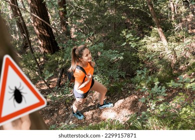 Mujer haciendo senderismo en el bosque de garrapatas infectadas con señal de advertencia. Riesgo de enfermedad transmitida por garrapatas y linces.