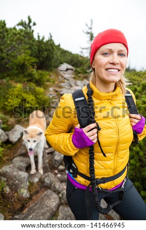 Woman hiking in mountains with akita dog, Karkonosze Mountain Range. Happy female hiker walking on mountain trail with backpack