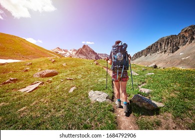 a woman hiking on a trail high in the mountains with a backpack and hiking poles