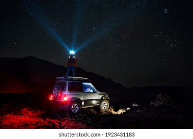 Woman with his head light is looking at the at starry night sky at off road car in the desert 