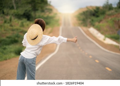 Woman hitchhiking on the road, empty rural curve, asphalt road way. Rear view.