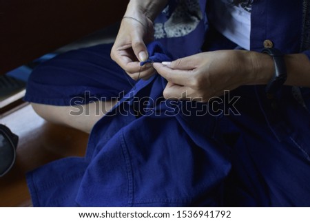 Woman hold a needle and thread for repair a blueshirt, darning shirts , repairing clothing.