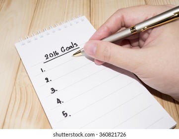 Woman hold a pen in her hand for write 2016 Goals in notebook on wood background (Business Concept)