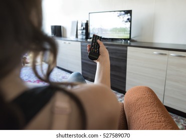 Woman Hold TV Remote Control. TV On The Background.
