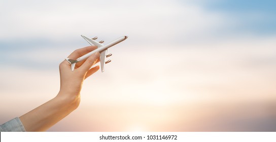 Woman holding airplane in hands and flying over the sunset background