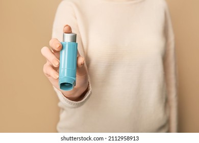 Woman Holding Asthma Inhaler On Brown Background