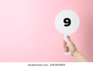 Woman holding auction paddle with number 9 on pink background, closeup. Space for text