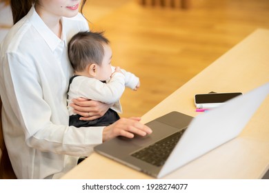 A Woman Holding A Baby And Operating A Laptop