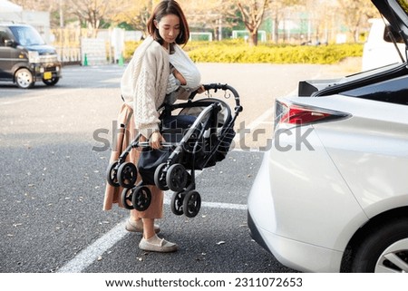 A woman holding a baby is taking out a stroller from the trunk of a car