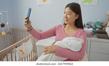 Woman holding baby while taking selfie in cozy bedroom surrounded by soft toys and a cradle, showcasing a happy moment in a nurturing home environment.