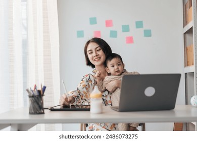 A woman is holding a baby while working on a laptop. The baby is wearing a white sweater and the woman is smiling. Concept of warmth and comfort, as the woman is able to balance her work - Powered by Shutterstock