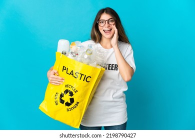 Woman Holding A Bag Full Of Bottles To Recycle Isolated On Blue Background Shouting With Mouth Wide Open