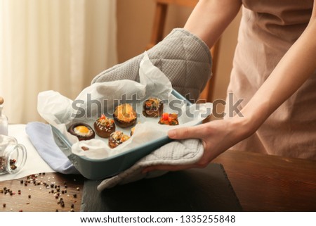 Woman holding baking dish with hot stuffed mushrooms in kitchen