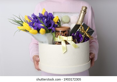 Woman holding basket with gifts, bouquet and champagne on light grey background, closeup - Shutterstock ID 1903172305