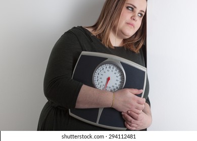 Woman holding a bathroom scale is leaning against wall with sad expression - Powered by Shutterstock