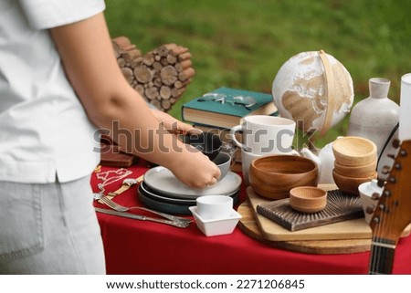 Woman holding beautiful bowls near table with different items on garage sale, closeup