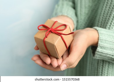 Frau, die ein schönes Weihnachtsgeschenk auf hellblauem Hintergrund hält, Nahaufnahme