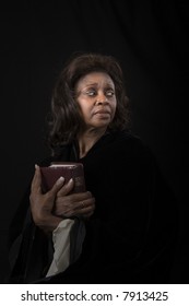 A Woman Holding A Bible To Her Chest And Looking To The Left On Black Background