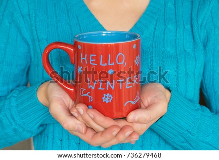 Woman holding a big red mug with written words Hello winter in her hands. 