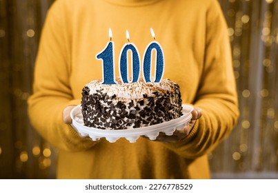 Woman holding birthday cake with number 100 candle, close up. One hundredth birthday or anniversary celebration. Copy space