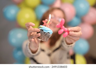 Woman Holding Birthday Cupcake With Candle and Balloon Animal While Smiling in the Background - Powered by Shutterstock