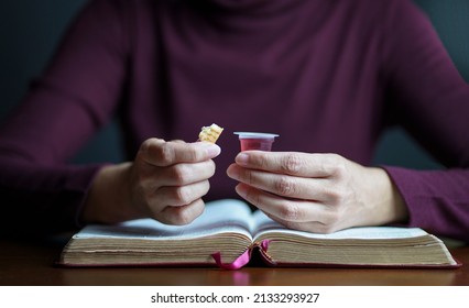 Woman holding biscuit and cup of wine with an open Bible on top of table, Taking Christian Holy Communion concept.
