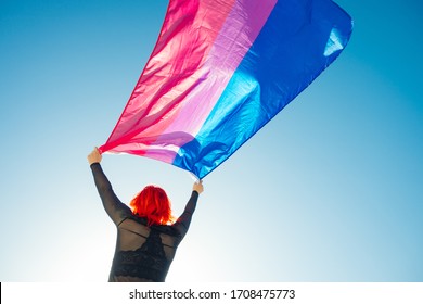 Woman holding the Bisexual Rainbow Flag with the blue sky in the background