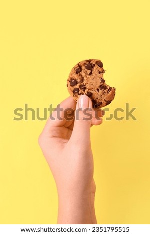 Woman holding bitten cookie with chocolate chips on yellow background