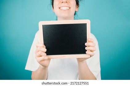 Woman holding a black board with blank space copy space for your text to camera while smiling happily. Mock up scene concept. Add your own text or image. Color background minimal concept.