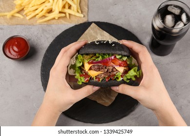 Woman holding black burger at served table, above view