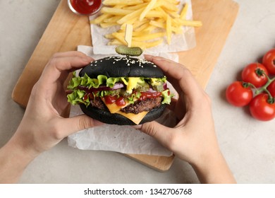 Woman holding black burger at served table, closeup