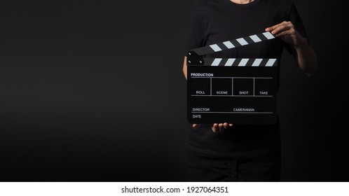 woman is holding black clapperboard or movie slate in studio shooting .It is use in video production and cinema industry on black background.