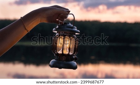 Woman Holding a Black Lantern, Hand holds a lamp in the dark, Lantern in twilight sky, Hand holding a lantern in a forest with blurred glowings.