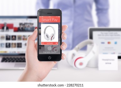 Woman Holding Black Mobile Smart Phone With Nfc Smart Pay Application On The Screen And Buying Headphones. Blurred Store With Different Devices On The Background. Concept Of Nfc Smart Pay Technology.