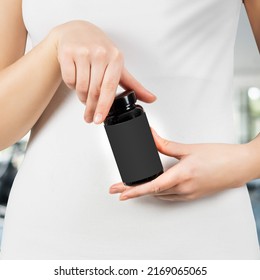 Woman holding black plastic jar in hands for cosmetics over white t shirt
