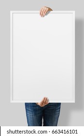 Woman Holding A Blank Poster With White Frame Mockup Isolated On A Gray Background. 