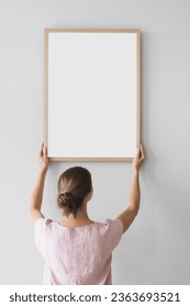 Woman holding blank wooden picture frame against a wall. Artwork mockup concept