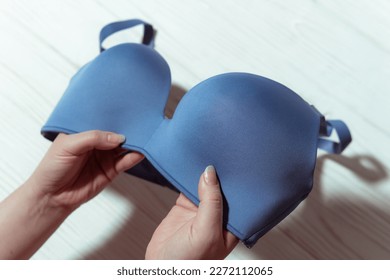 Woman holding blue bra, wooden background, closeup. Womens underwear.