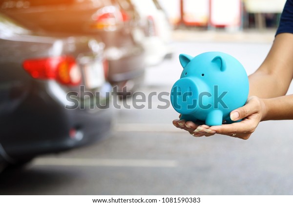 woman holding blue piggy\
bank with standing near the car for save money to buy vehicle\
& insurance
