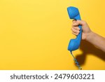 Woman holding blue telephone handset on yellow background, closeup. Space for text