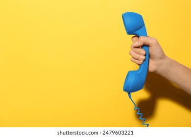 Woman holding blue telephone handset on yellow background, closeup. Space for text