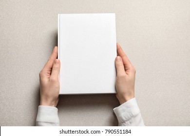 Woman holding book with blank cover on light background. Mock up for design