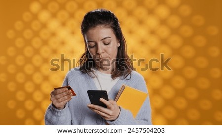 Woman holding books, purchasing more with phone, conveying joy of reading concept, studio background. Person buying novels online with credit card, showing appreciation for literature, camera B