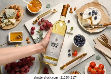 Woman holding bottle of white wine at grey table with snacks, top view - Powered by Shutterstock