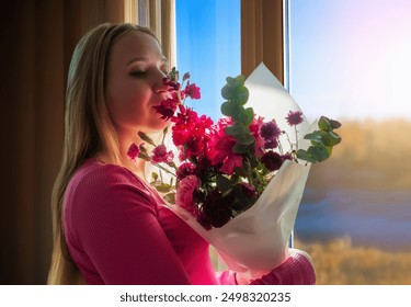 A woman is holding a bouquet of flowers and smelling them. The flowers are pink and white, and the woman is smiling. Scene is happy and peaceful, as the woman is enjoying the beauty of the flowers - Powered by Shutterstock