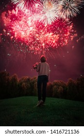 A Woman Holding Bouquet Of Flowers, Watching The Beautiful Holiday Fireworks On The Green Grass Hill. Summer Celebration.  Background For 4th Of July 