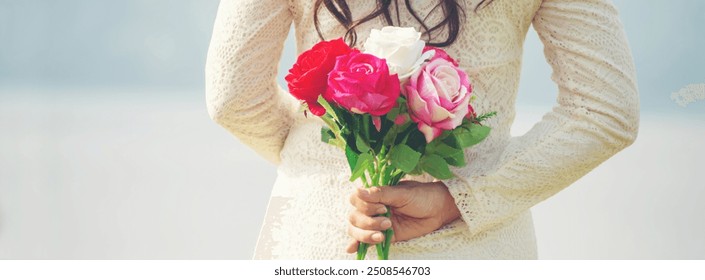 Woman holding bouquet of roses behind back. Back view of Woman in white lace dress holding a colorful flower.- love and surprise concept-banner image. - Powered by Shutterstock