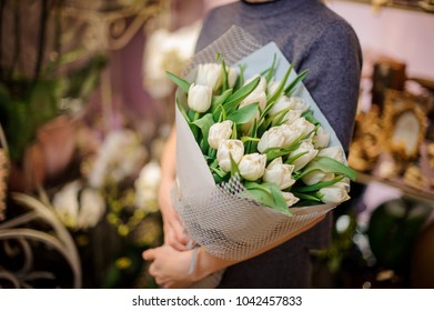 Woman Holding A Bouquet Of White Tulips Wrapped In A Grey Paper On The Background Of Flower Shop