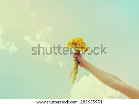 Woman holding bouquet of yellow dandelions on background of sky in summer, close-up of hand with flowers. Image with instagram color effect