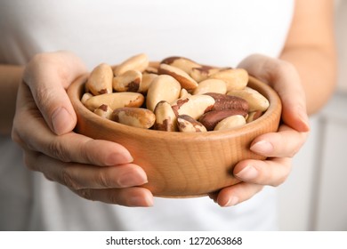 Woman Holding Bowl With Brazil Nuts On Blurred Background, Closeup